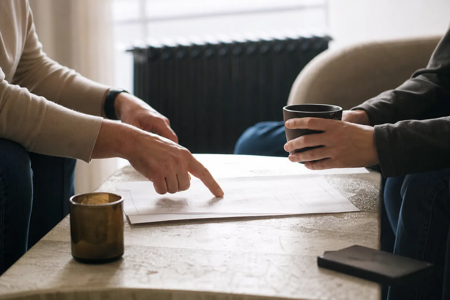 Deux personnes échangeant autour d’un document posé sur une table basse, mains visibles