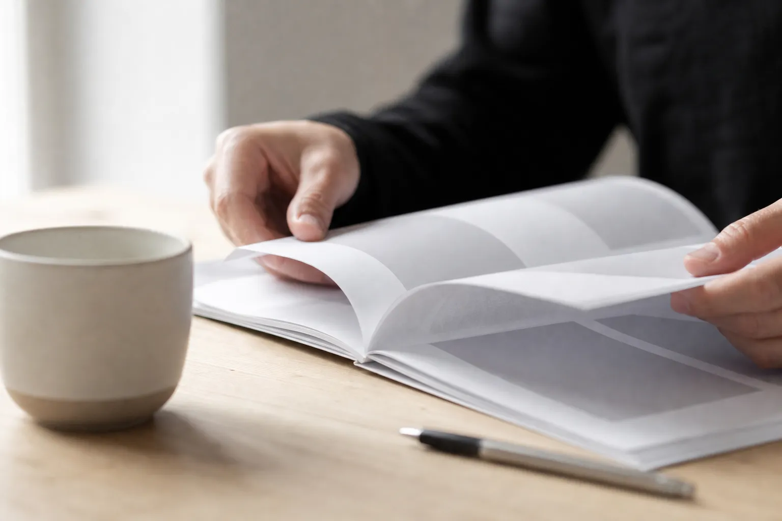 Mains qui feuillettent un document patrimonial sur une table en bois clair, lumière naturelle